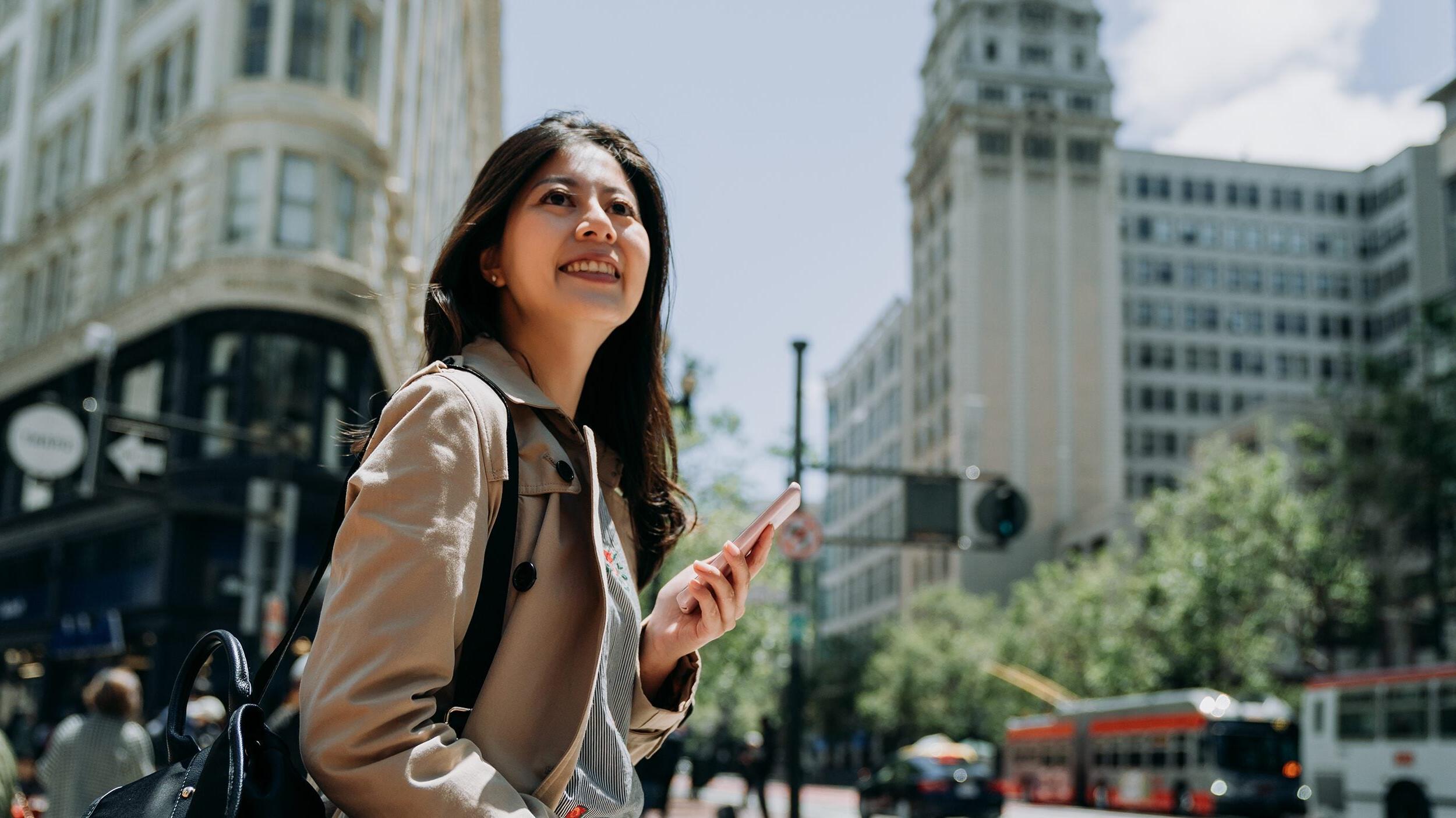 Happy woman holding phone in busy city area in San Francisco.