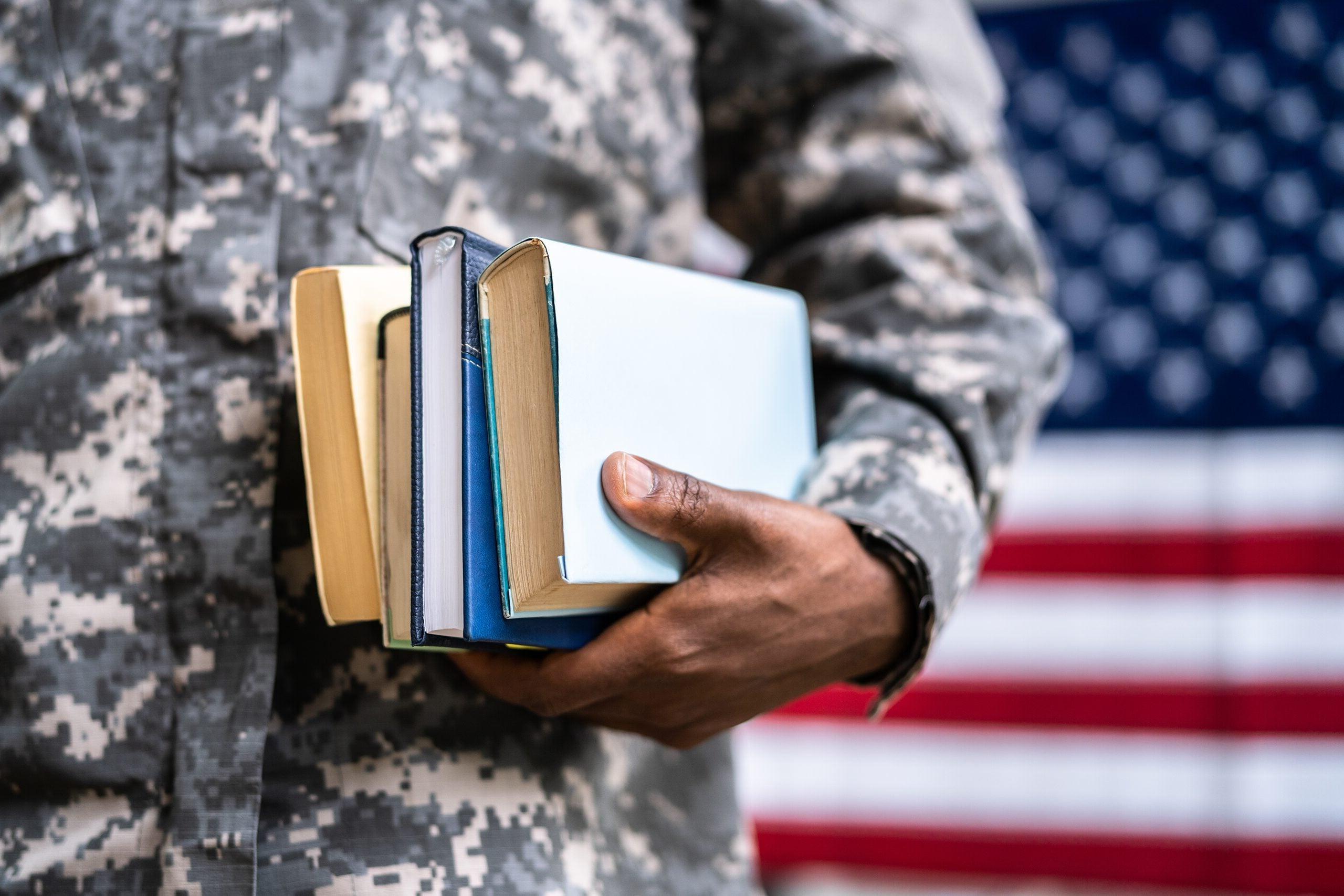 军校学生拿着书站在美国国旗前.
